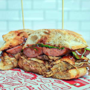 Pulled pork, smoked pork belly, pit sausage, bbq sauce, pickled onion, arugula, and chili lime mayonnaise on a ciabatta. **contains wheat, soy, egg, fish**