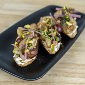 Roasted grape bruschetta with creamy ricotta, hot honey, pickled shallots, pistachios and fresh basil on toasted baguette.